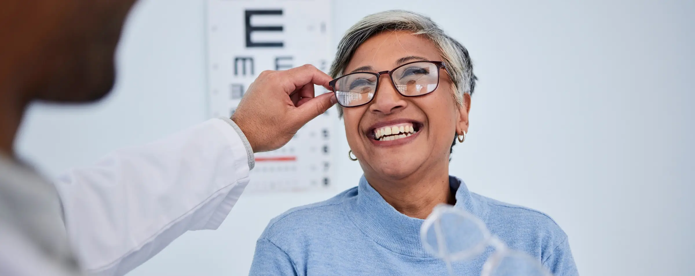 Joyful older woman being fitted for prescription eyeglasses by optical team